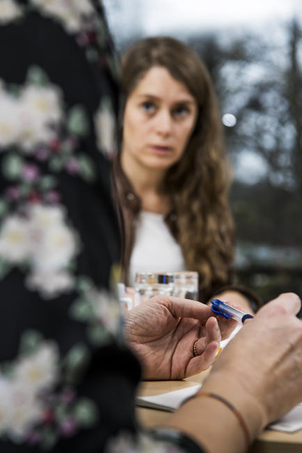 Hænder ved skrivebord med person i baggrunden