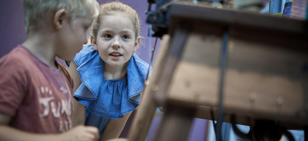 Børn der undersøger en maskine fra en tekstilfabrik. 