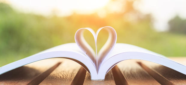 En bog ligger oplåset på et havebord udenfor i solnedgang. Midtersiderne er foldet som et hjerte.