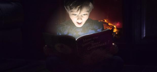 Dreng sidder i mørkt rum med bog der lyser op i hans overraskede ansigt