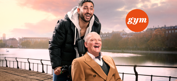 En ung mand skubber en ældre mand i kørestol ved søerne i København, de griner sammen