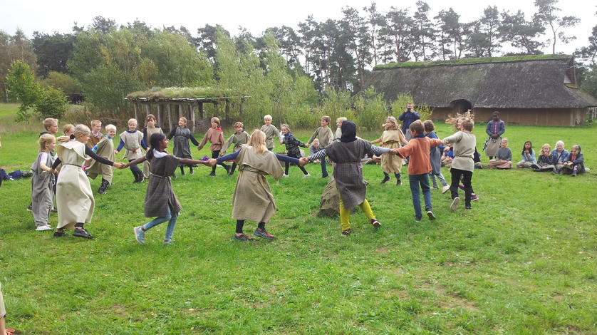 Børn danser i rundkreds i Hvolris Jernalderlandsby.