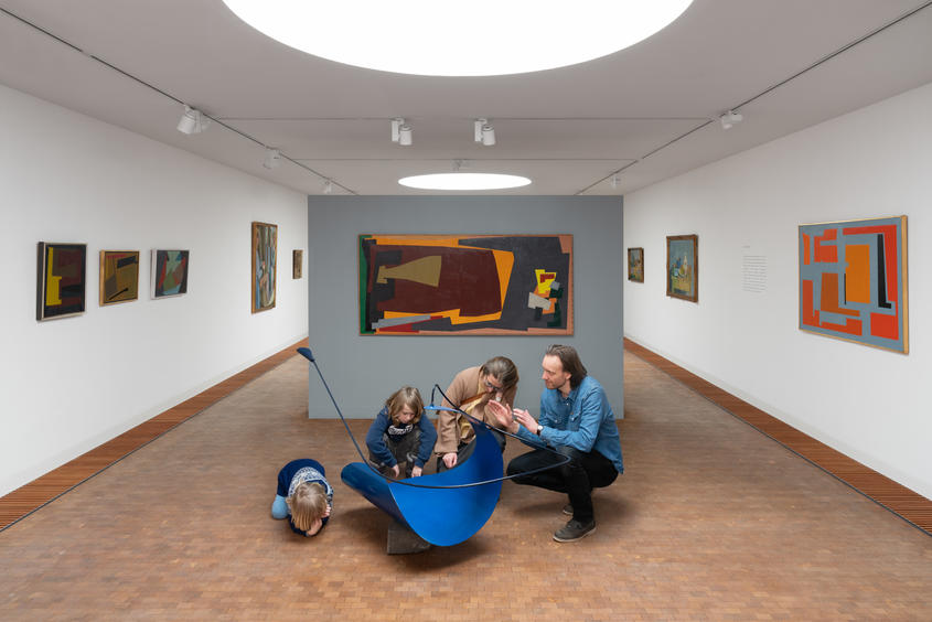 Foto indefra museet, hvor en far, mor og børn taler om en blå skulptur